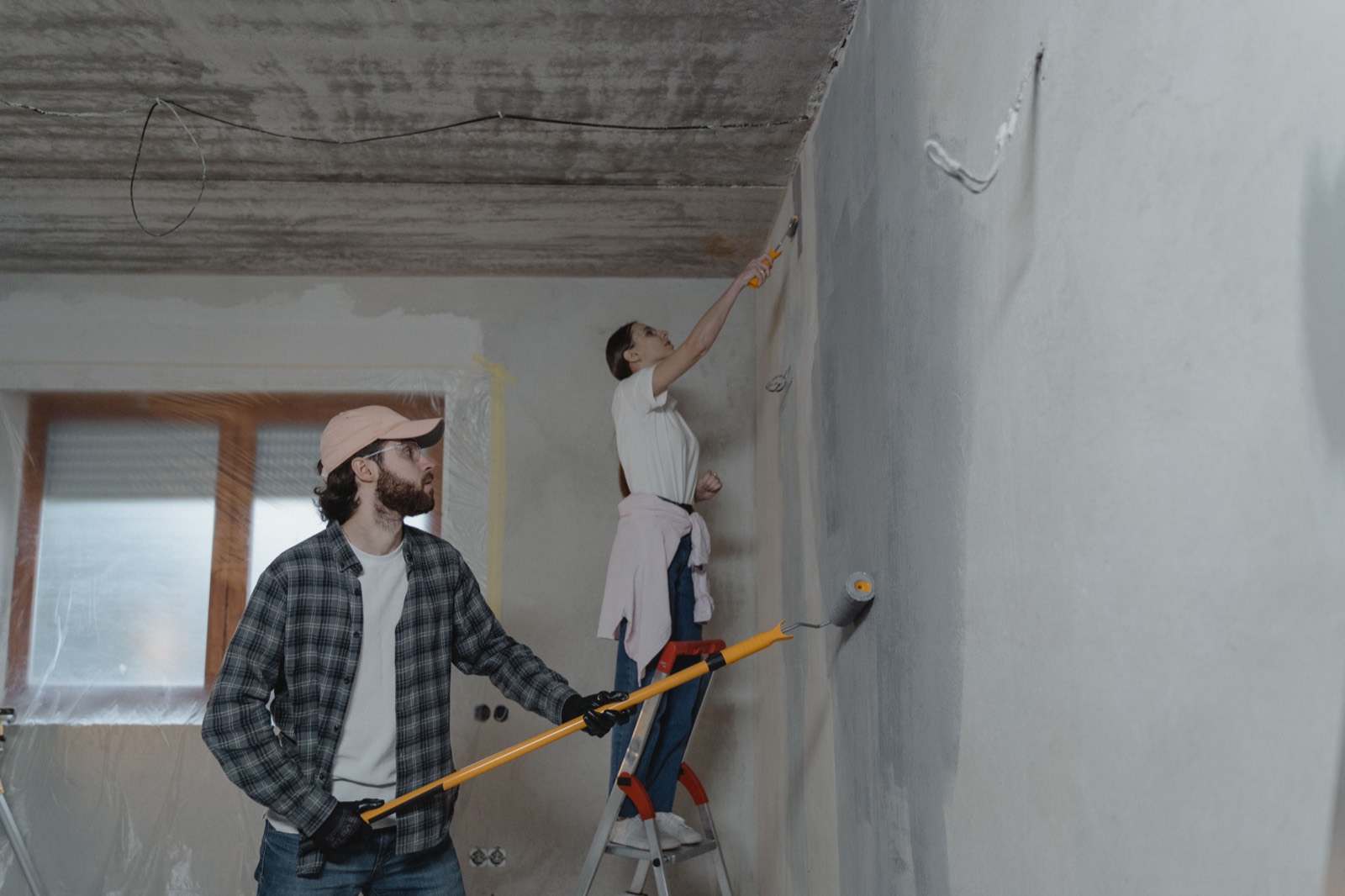 Two painters finishing a room, one rolling the wall from a stepladder
